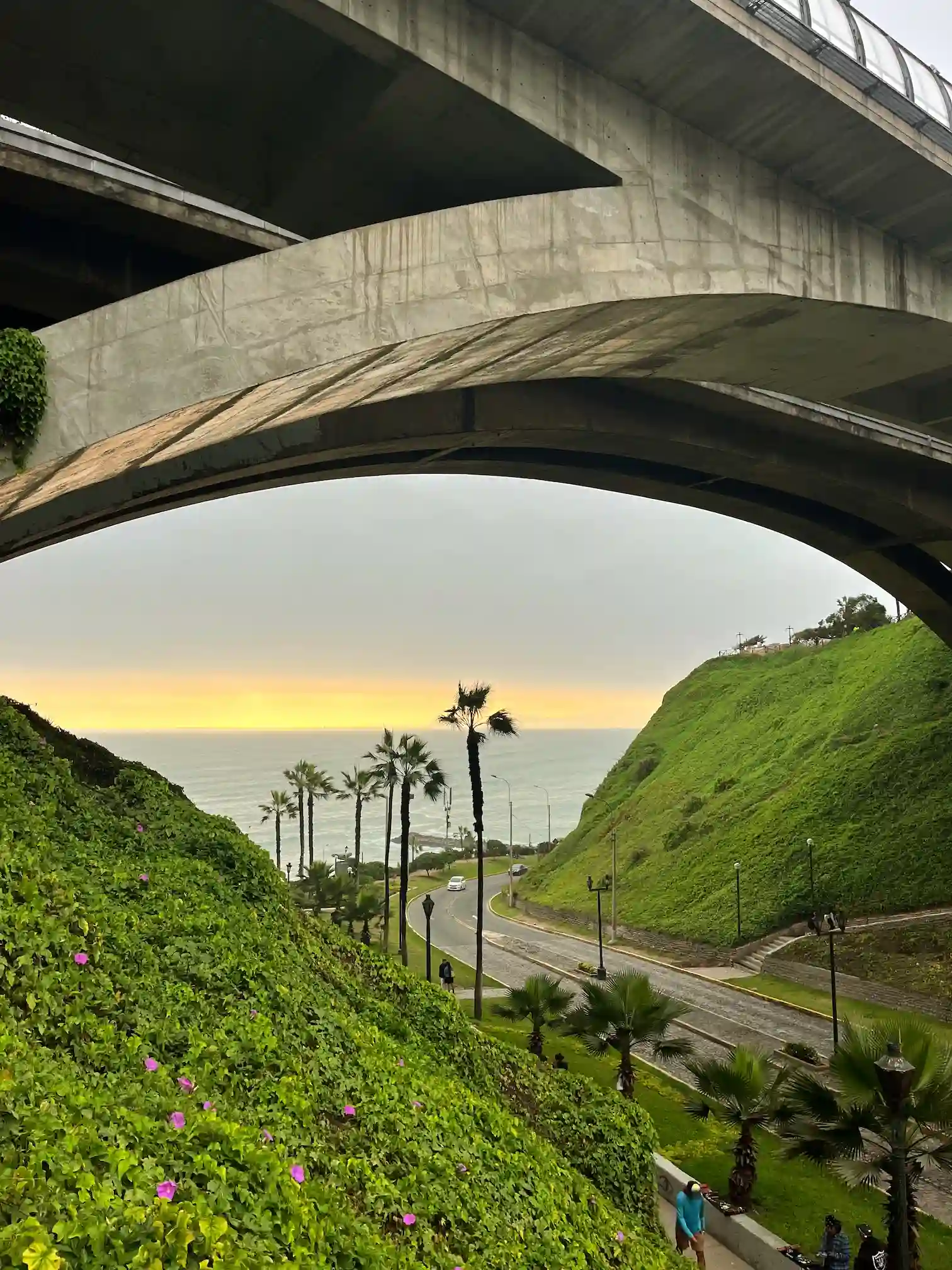Pakrantės panorama pro tilto arką su palmėmis ir saulėlydžiu, Miraflores, Lima