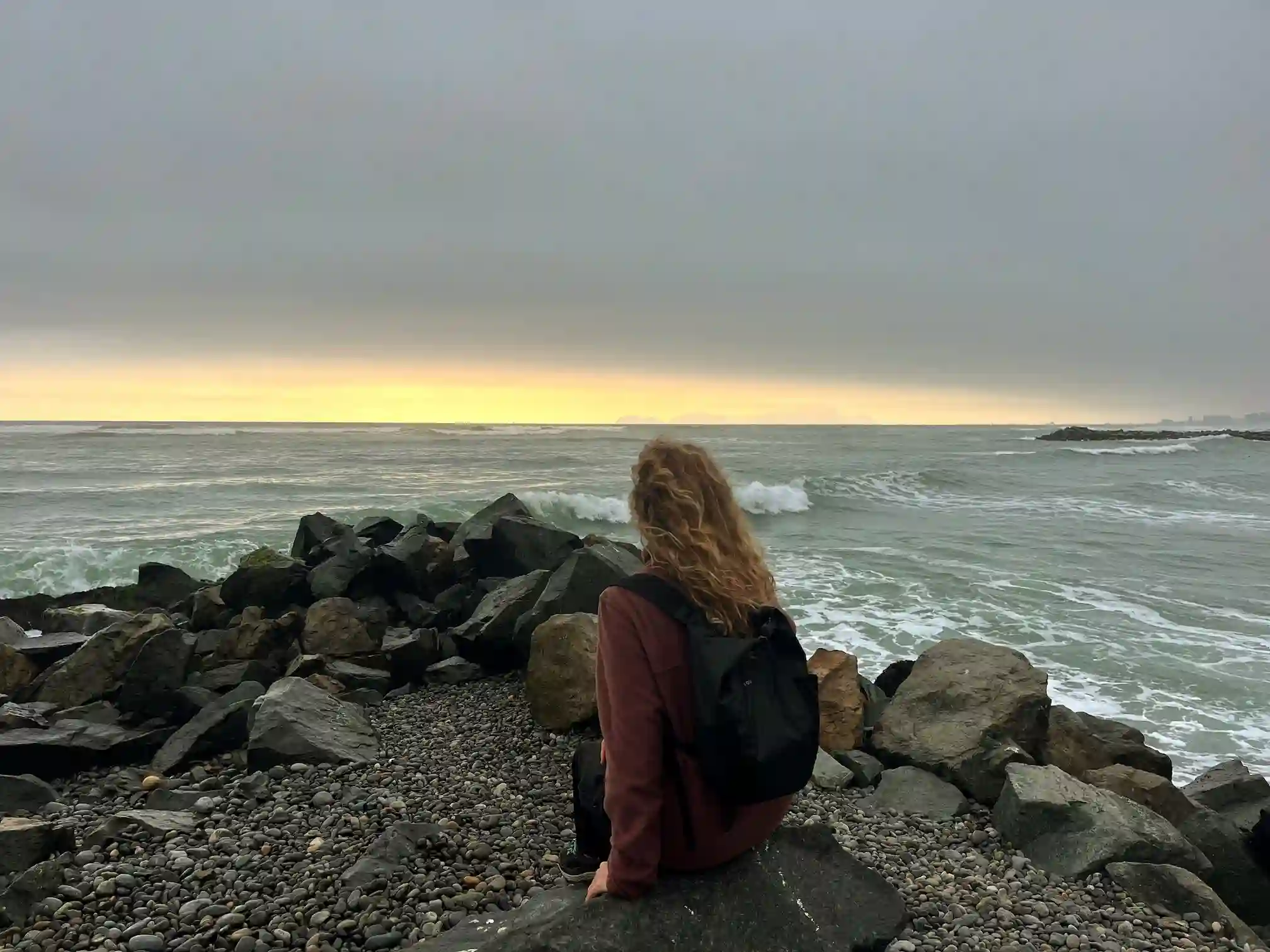 Moteris sėdi ant uolų ir stebi Ramiojo vandenyno bangas saulėlydžio metu, Lima