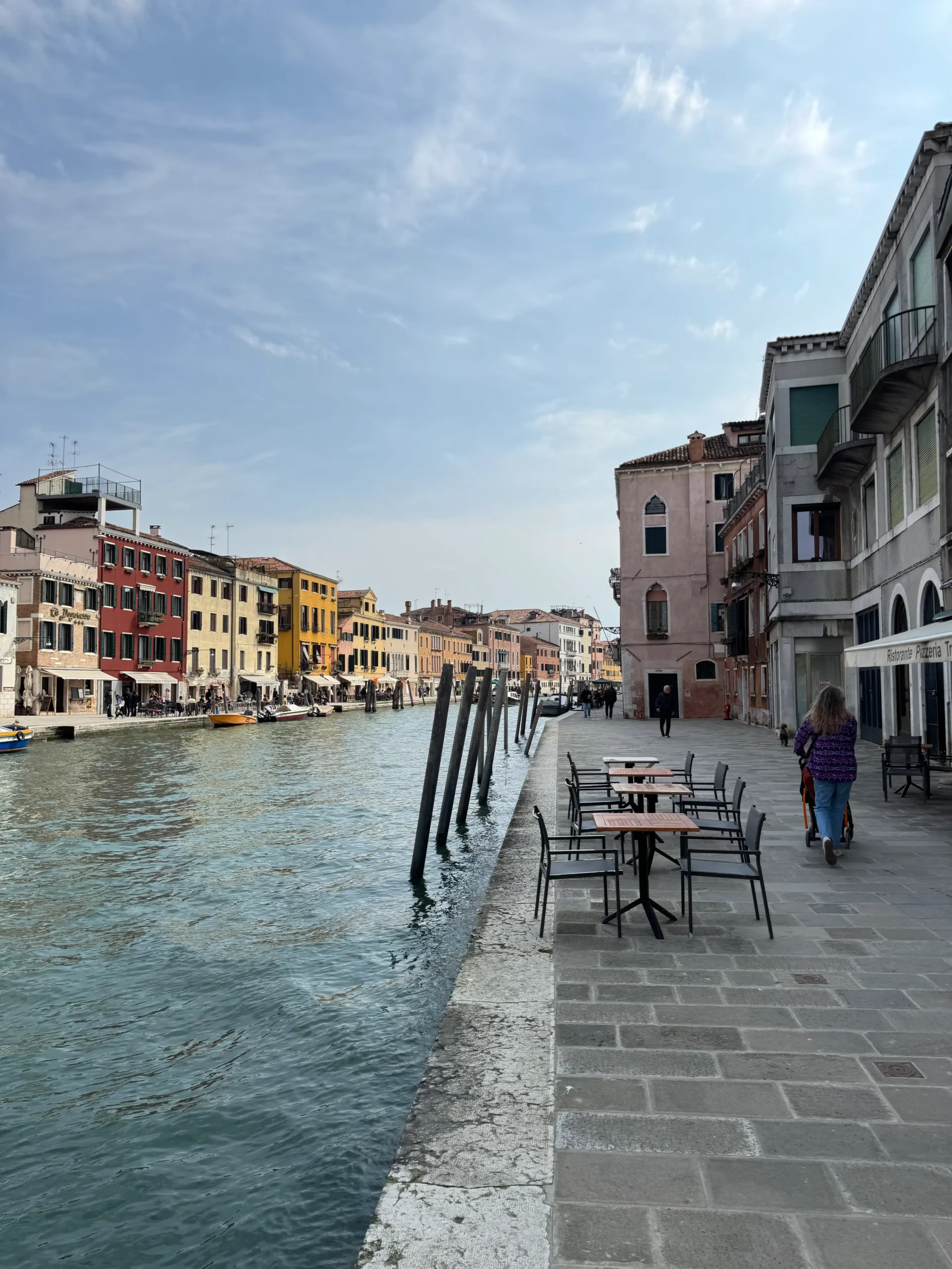 Venecijos kanalas su spalvingais pastatais ir kavinės terasėlė ant vandens kranto, Italija