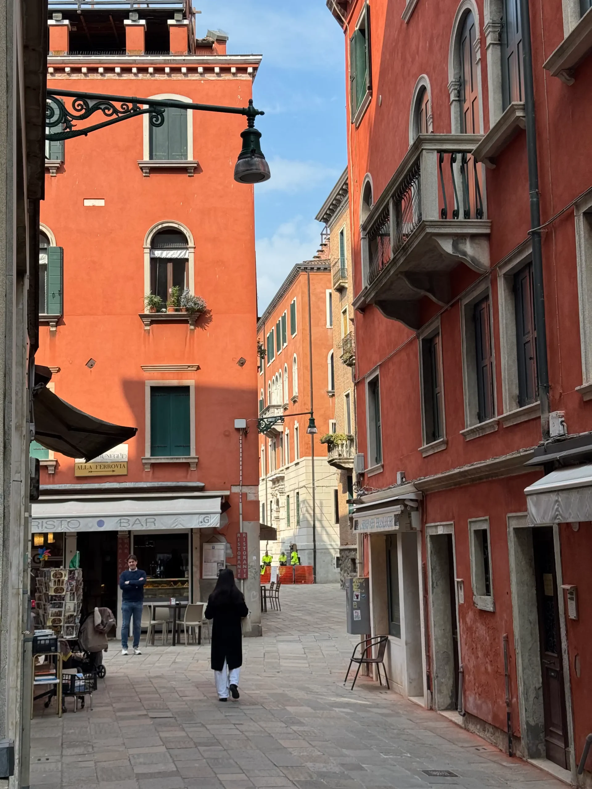 Siauros Venecijos gatvelės su ryškiai oranžiniais pastatais ir tradicine žibinto laikiklio geležimi
