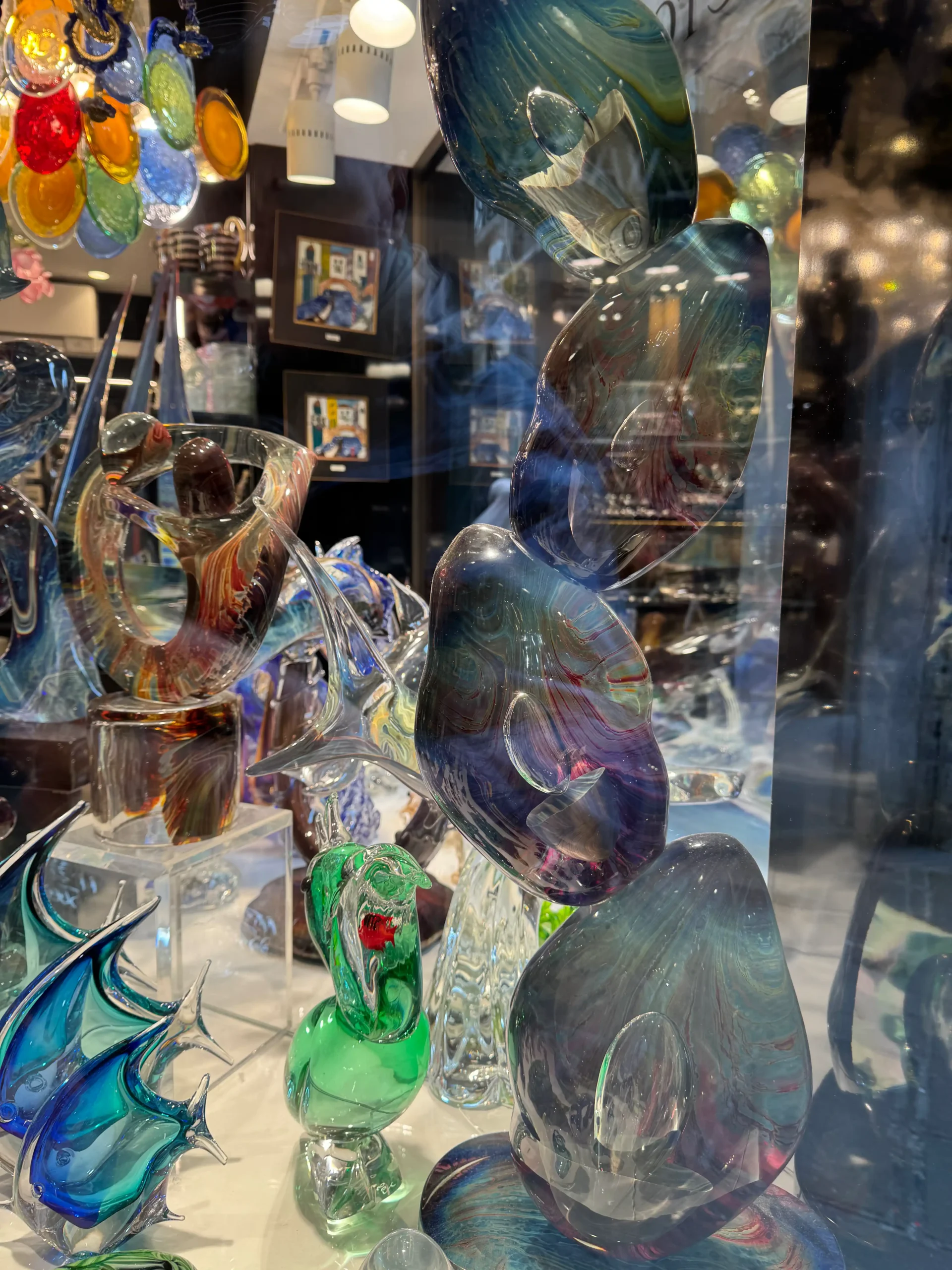 Murano stiklo figūrėlės parduotuvės vitrinoje – spalvingi žuvys, žmonių skulptūros ir dekoratyviniai dirbiniai