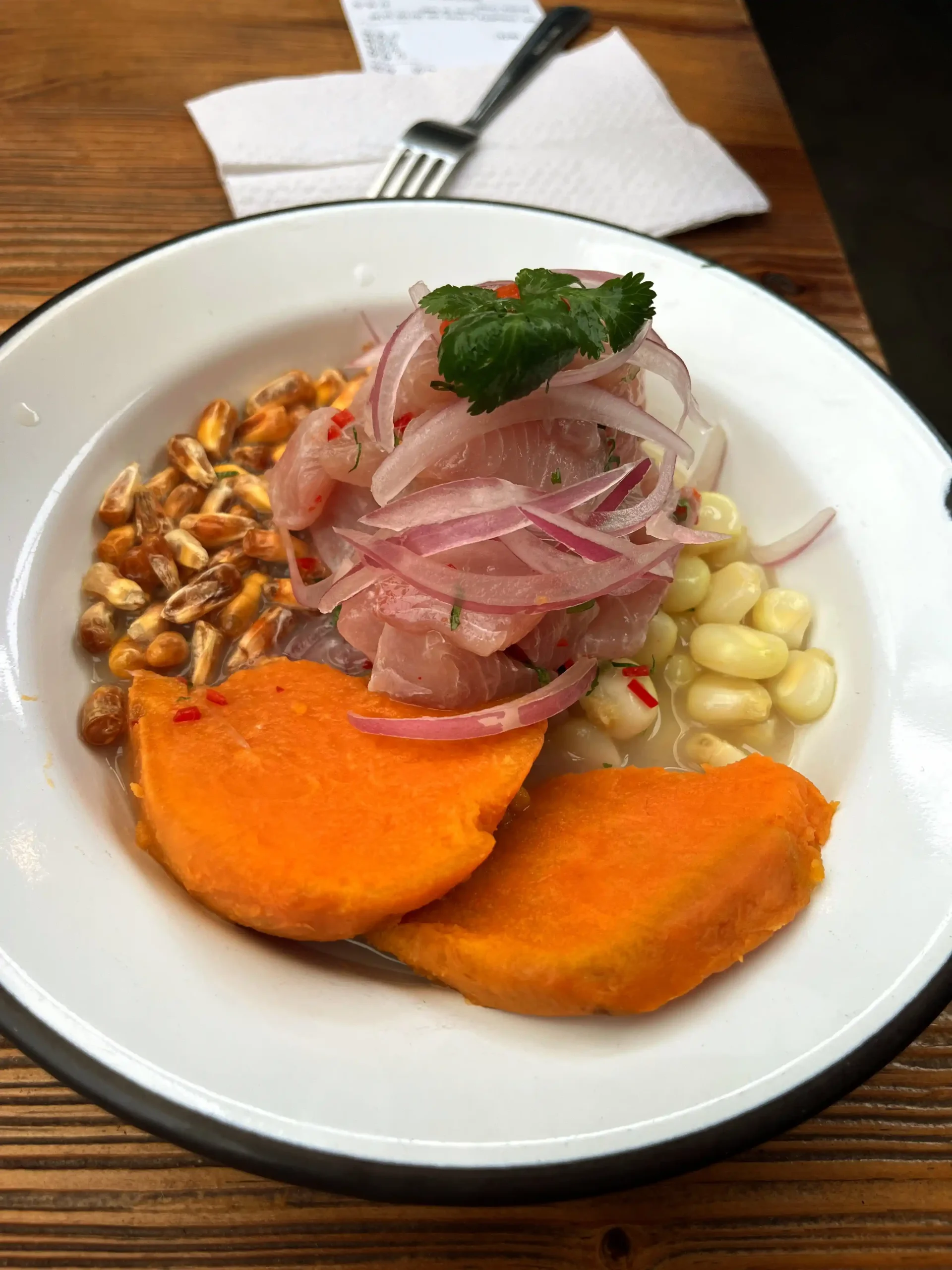 Peruietiškas ceviche su šviežia žuvimi, raudonaisiais svogūnais, batatu, kukurūzais ir skrudinta kukurūzų kančija baltame dubenyje