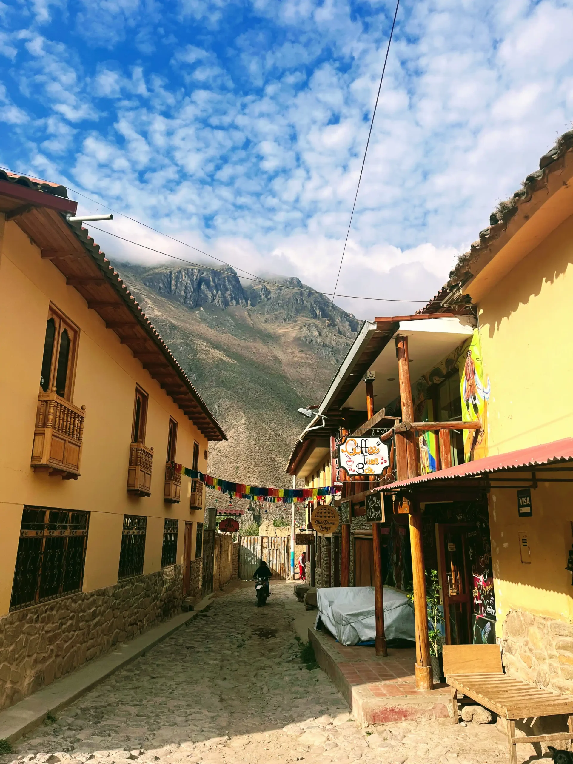 Akmenimis grįsta Ollantaytambo gatvelė su geltonais namais ir Anų kalnais Šventajame slėnyje