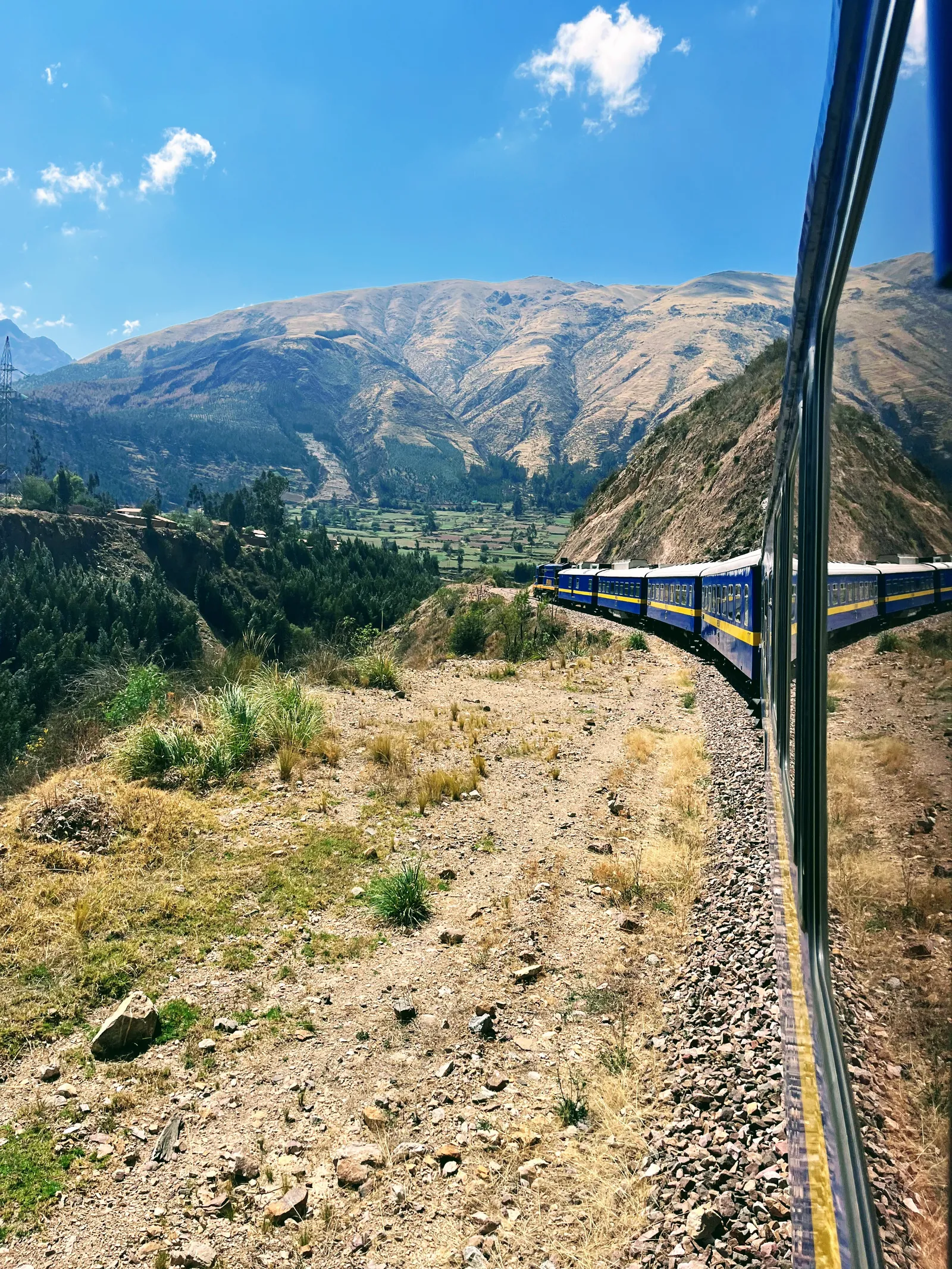 Mėlynas Andean Explorer traukinys vingiuoja Andų kalnų slėniu pakeliui į Puną, vaizdas pro vagono langą