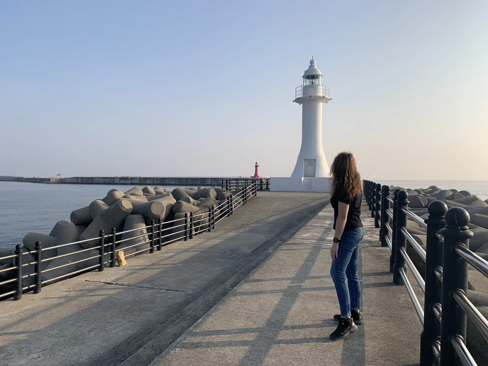 Moteris prie balto švyturio ant molo Jeju saloje giedrą vakarą