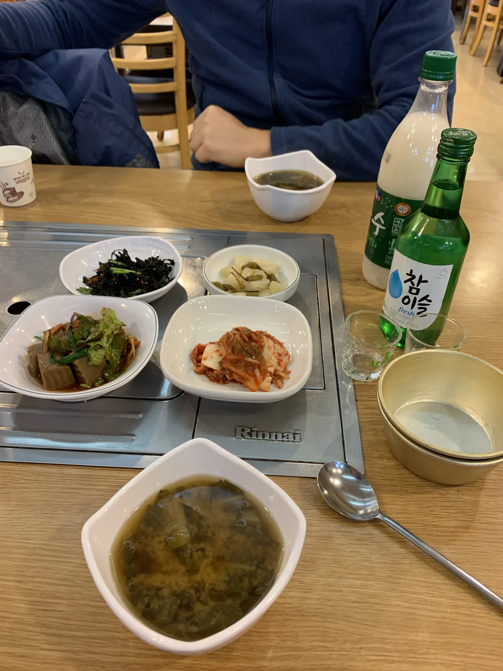Restorano stalas su banchan priedais, sriuba ir žaliu soju buteliuku