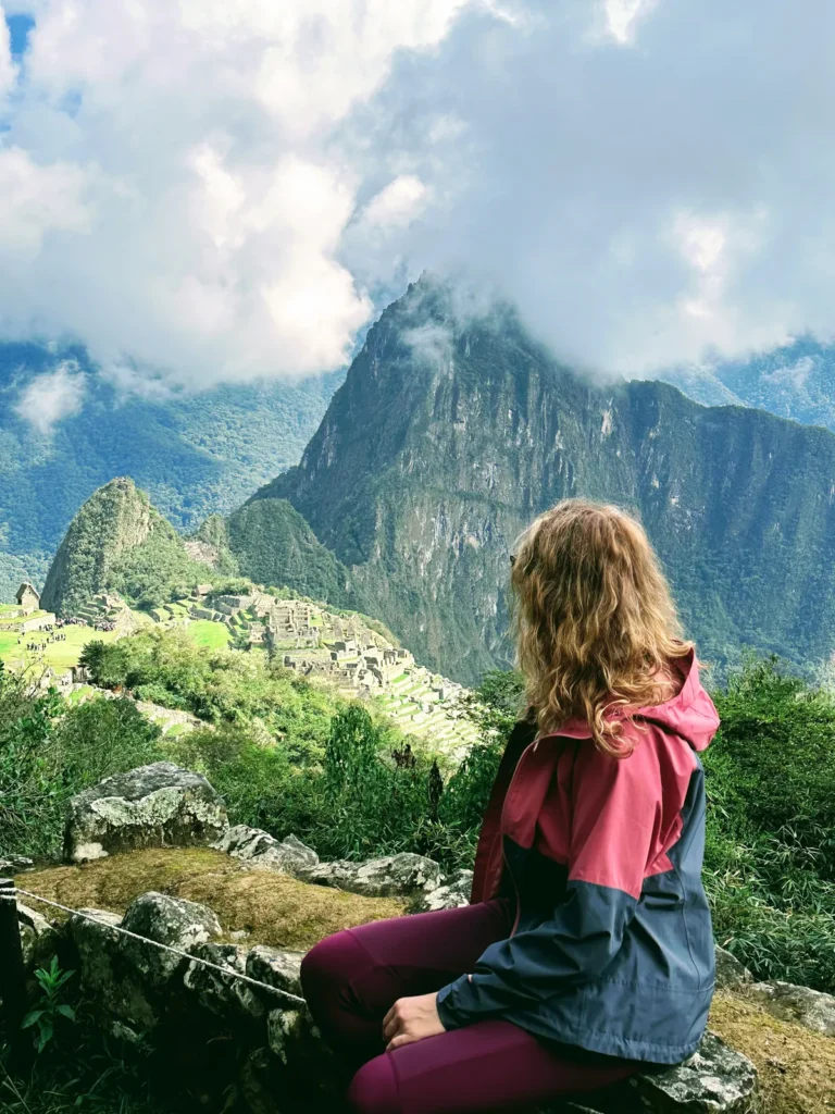 Inca Trail alternatyvos: kaip pasiekti Maču Pikču be leidimų loterijos Keliautoja sėdi ir žiūri į Maču Pikču ir apsiniaukusias Andų viršukalnes